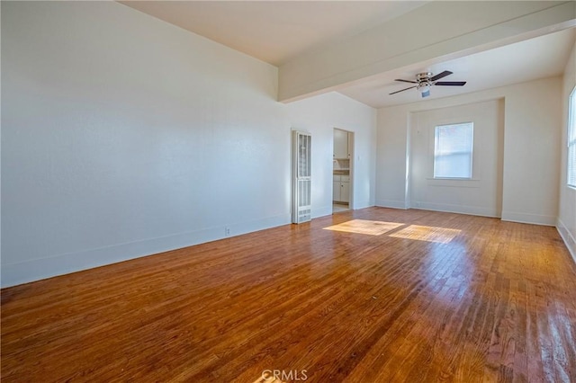 empty room with beamed ceiling, hardwood / wood-style floors, and ceiling fan