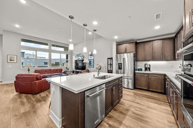 kitchen with pendant lighting, sink, stainless steel appliances, a center island with sink, and decorative backsplash