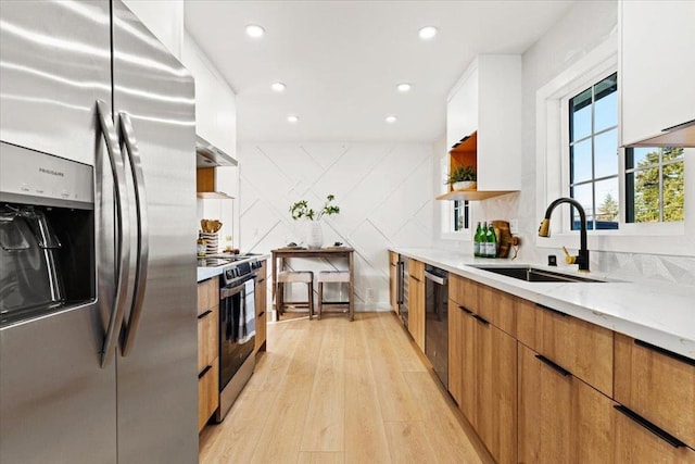 kitchen with sink, white cabinetry, stainless steel appliances, light stone counters, and light wood-type flooring