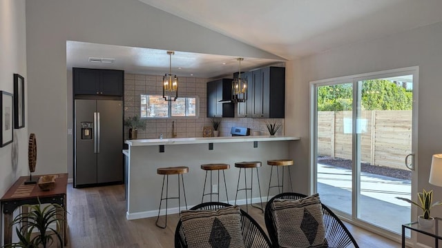 kitchen with a kitchen bar, decorative light fixtures, stainless steel fridge, kitchen peninsula, and decorative backsplash