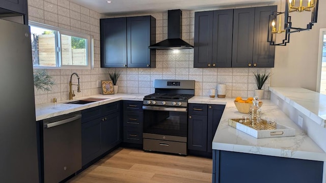 kitchen featuring sink, hanging light fixtures, stainless steel appliances, wall chimney range hood, and light wood-type flooring