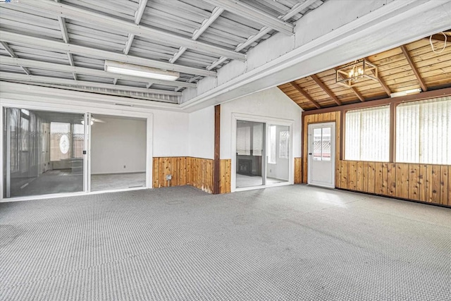 carpeted spare room with an inviting chandelier, lofted ceiling, and wooden walls