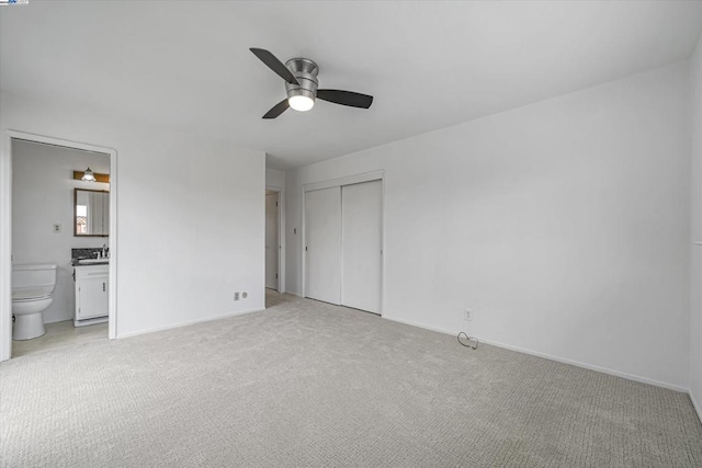 unfurnished bedroom featuring sink, ceiling fan, ensuite bathroom, light colored carpet, and a closet