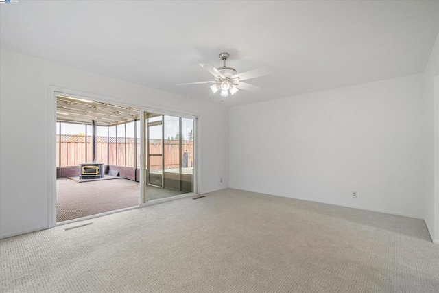 carpeted spare room with a wood stove and ceiling fan