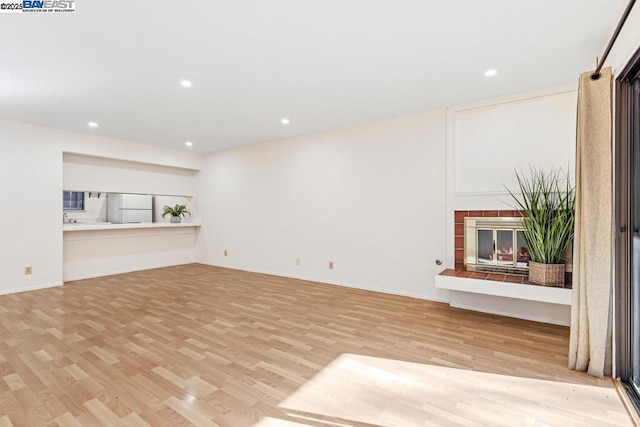 unfurnished living room with a tiled fireplace and light wood-type flooring