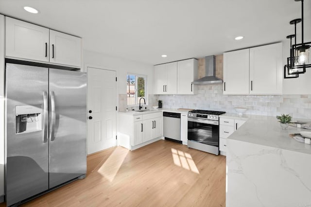 kitchen featuring decorative light fixtures, white cabinetry, sink, stainless steel appliances, and wall chimney exhaust hood