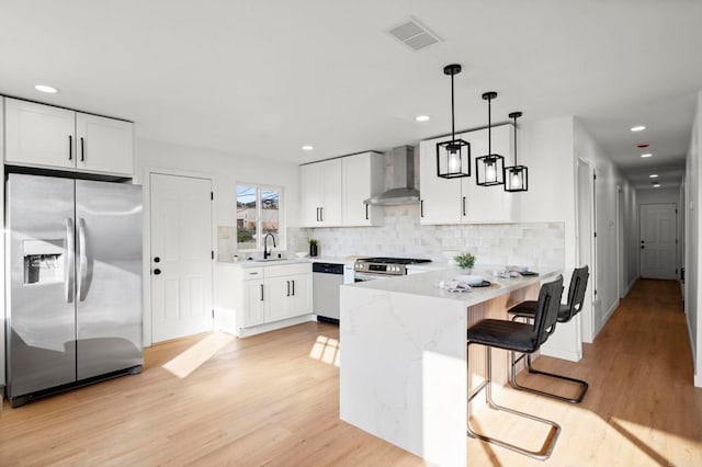 kitchen with stainless steel appliances, white cabinetry, pendant lighting, and wall chimney exhaust hood