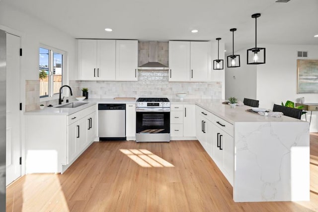 kitchen featuring sink, stainless steel appliances, white cabinets, kitchen peninsula, and wall chimney exhaust hood