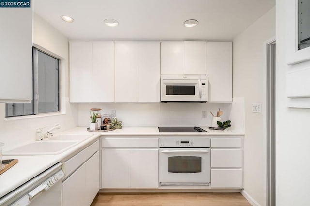 kitchen with sink, white appliances, light hardwood / wood-style floors, and white cabinets