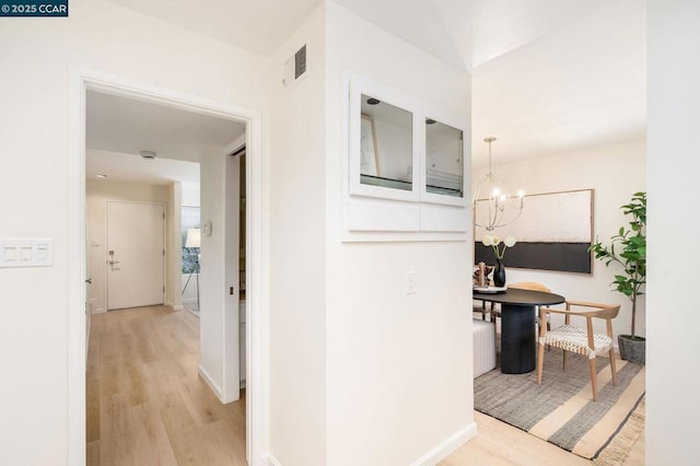 hall with light hardwood / wood-style floors and a notable chandelier