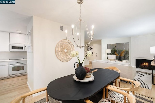 dining space featuring light hardwood / wood-style flooring, a fireplace, and a chandelier