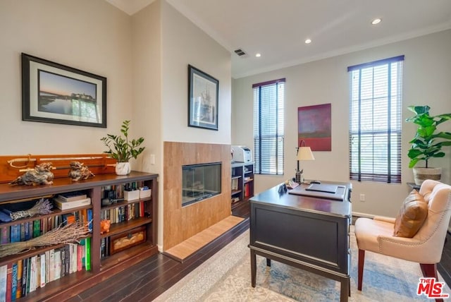 home office featuring dark wood-type flooring, ornamental molding, and a tiled fireplace