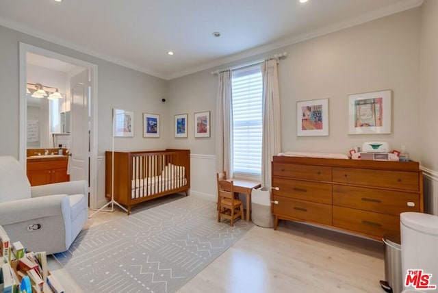 bedroom featuring ornamental molding, ensuite bathroom, light hardwood / wood-style floors, and a crib