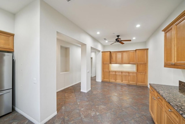 kitchen featuring ceiling fan, dark stone counters, and stainless steel fridge