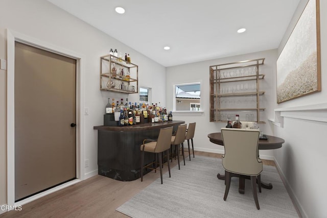 bar featuring recessed lighting, baseboards, a bar, and wood finished floors