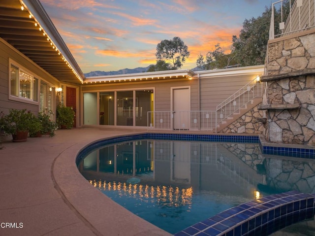 pool at dusk with a patio area, an outdoor pool, and stairs