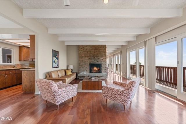 living room with dark wood finished floors, beamed ceiling, a fireplace, and a textured ceiling