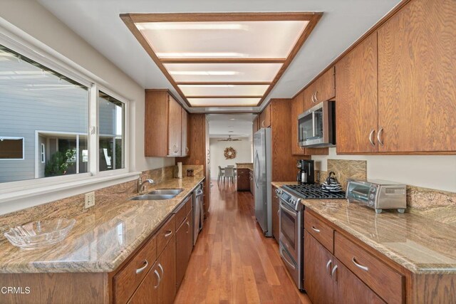 kitchen with a sink, stainless steel appliances, brown cabinets, and light wood-type flooring