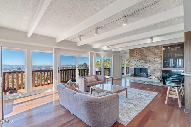 living room with wood finished floors, a fireplace, track lighting, a textured ceiling, and beamed ceiling