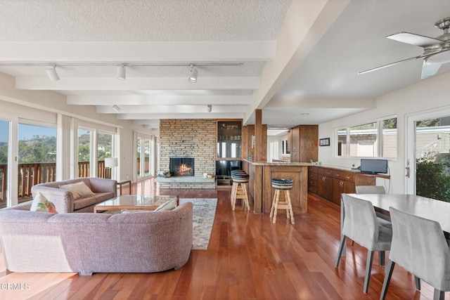 living room with beamed ceiling, wood-type flooring, a wealth of natural light, and a textured ceiling