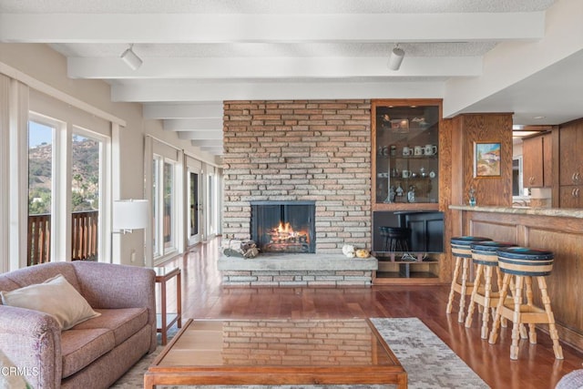 living room with a large fireplace, wood walls, beam ceiling, wood finished floors, and a textured ceiling