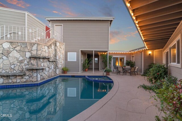 pool at dusk featuring a patio, stairway, and a pool with connected hot tub