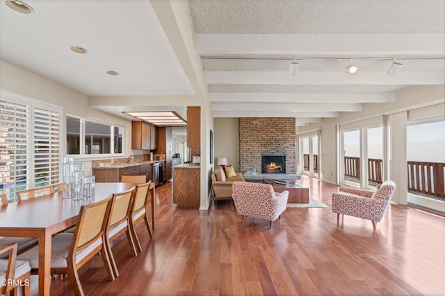 living area featuring a large fireplace, beam ceiling, a textured ceiling, and wood finished floors