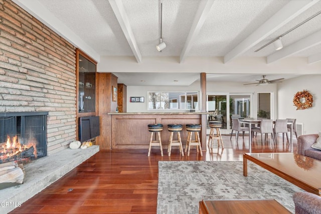 living area with track lighting, a large fireplace, beam ceiling, wood finished floors, and a textured ceiling