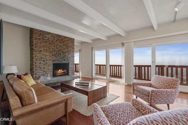 living area with wood finished floors, baseboards, beam ceiling, a fireplace, and a textured ceiling