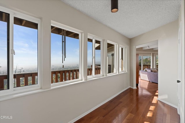 hallway with dark wood finished floors, a textured ceiling, and baseboards