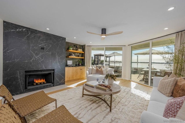 living room featuring ceiling fan, light hardwood / wood-style flooring, a fireplace, and a wall of windows