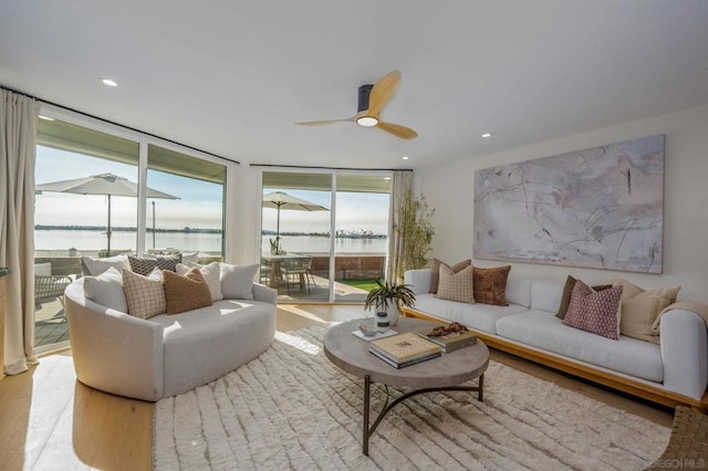 living room featuring light wood-type flooring, expansive windows, ceiling fan, and a water view