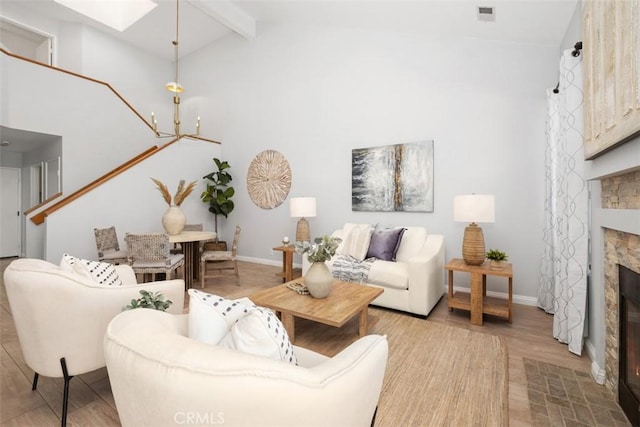 living room with a notable chandelier, a fireplace, light hardwood / wood-style floors, and vaulted ceiling with skylight