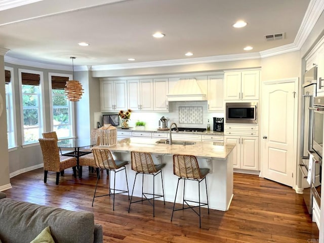 kitchen with a breakfast bar, stainless steel microwave, visible vents, dark wood-type flooring, and a sink