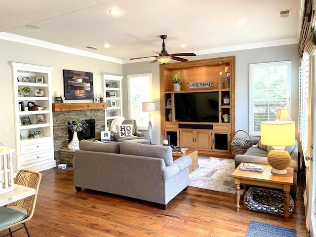 living room with a fireplace, visible vents, wood finished floors, and ornamental molding