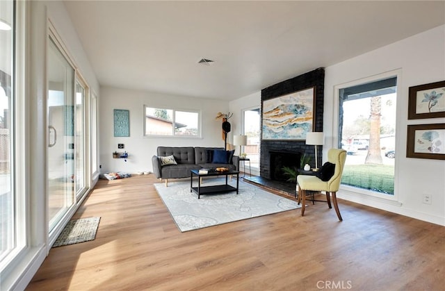 living room with a brick fireplace, light hardwood / wood-style floors, and a healthy amount of sunlight