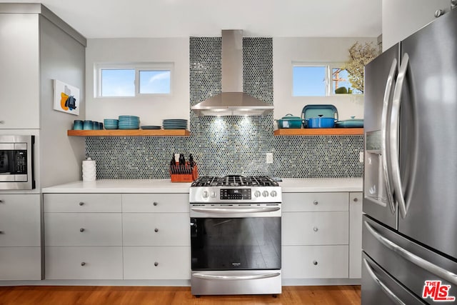 kitchen with stainless steel appliances, tasteful backsplash, plenty of natural light, and wall chimney range hood