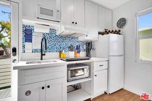 kitchen with sink, white appliances, white cabinetry, tasteful backsplash, and light wood-type flooring