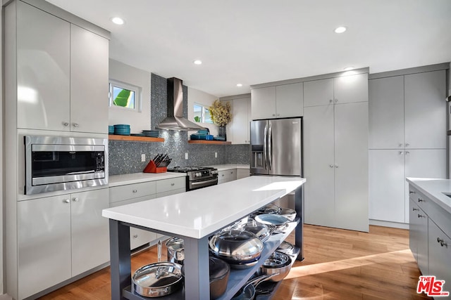 kitchen with stainless steel appliances, gray cabinetry, wall chimney range hood, and light wood-type flooring