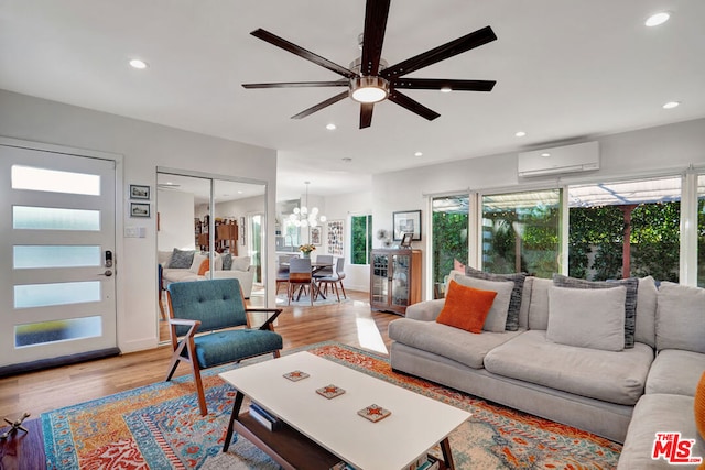 living room with light wood-type flooring, ceiling fan with notable chandelier, and a wall unit AC