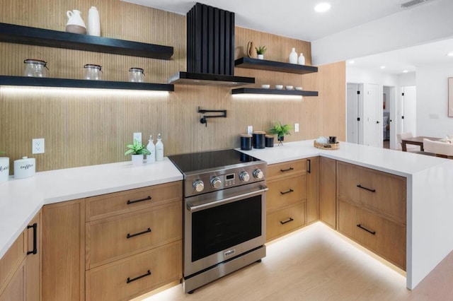 kitchen with ventilation hood, high end stove, light hardwood / wood-style floors, and kitchen peninsula