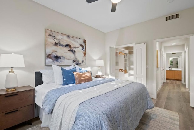 bedroom featuring hardwood / wood-style flooring, ensuite bathroom, a walk in closet, and ceiling fan