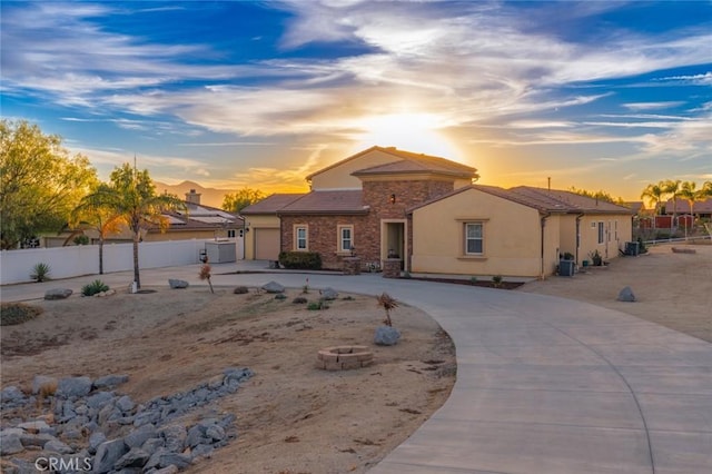 exterior space featuring stucco siding, an attached garage, fence, driveway, and stone siding