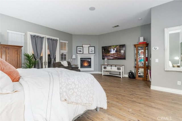 bedroom with visible vents, a warm lit fireplace, baseboards, and light wood finished floors