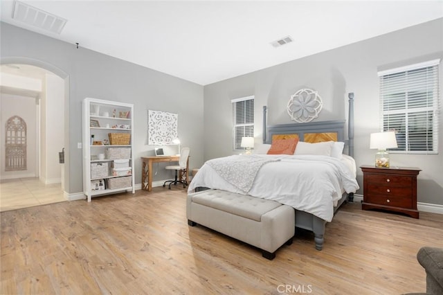 bedroom with baseboards, light wood finished floors, visible vents, and arched walkways