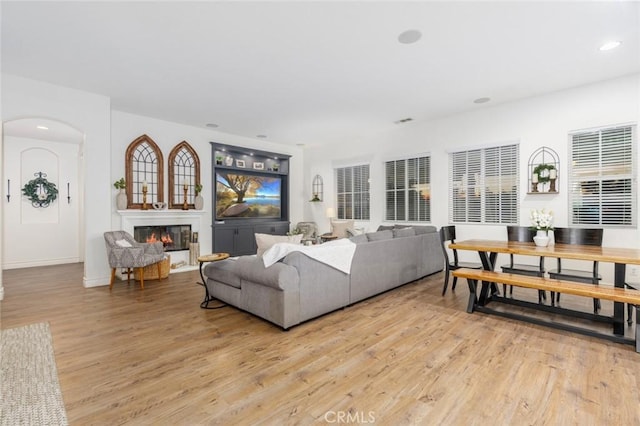 living room with arched walkways, recessed lighting, light wood finished floors, and a glass covered fireplace