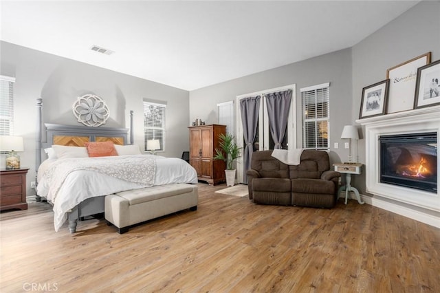 bedroom with baseboards, visible vents, a glass covered fireplace, and light wood-type flooring