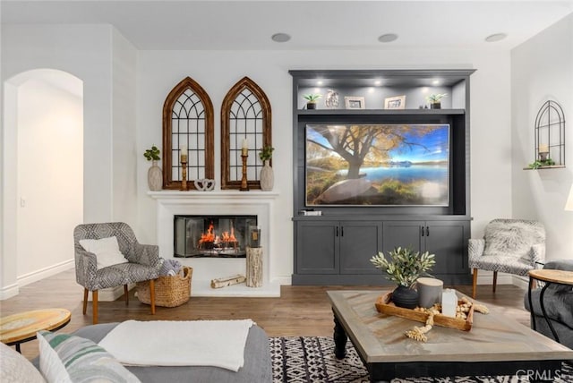 sitting room with baseboards, a glass covered fireplace, arched walkways, and light wood-type flooring