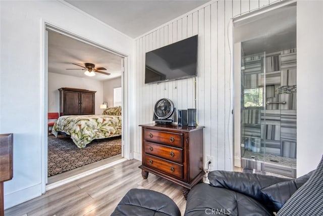 bedroom featuring ceiling fan, light hardwood / wood-style flooring, and wood walls