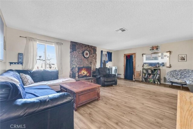 living room with a stone fireplace, light wood-type flooring, and a textured ceiling